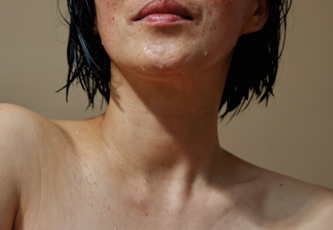 A close-up of a person's neck, jawline, and wet shoulders, showing glistening skin with water droplets, highlighting a fresh and deeply hydrated look.