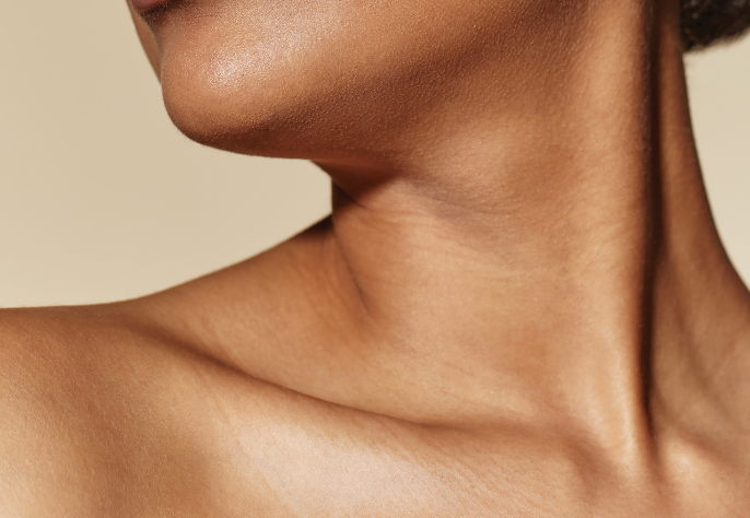 A close-up of a person's neck, jawline, and bare shoulder with clear, smooth, and healthy-looking skin against a light background.